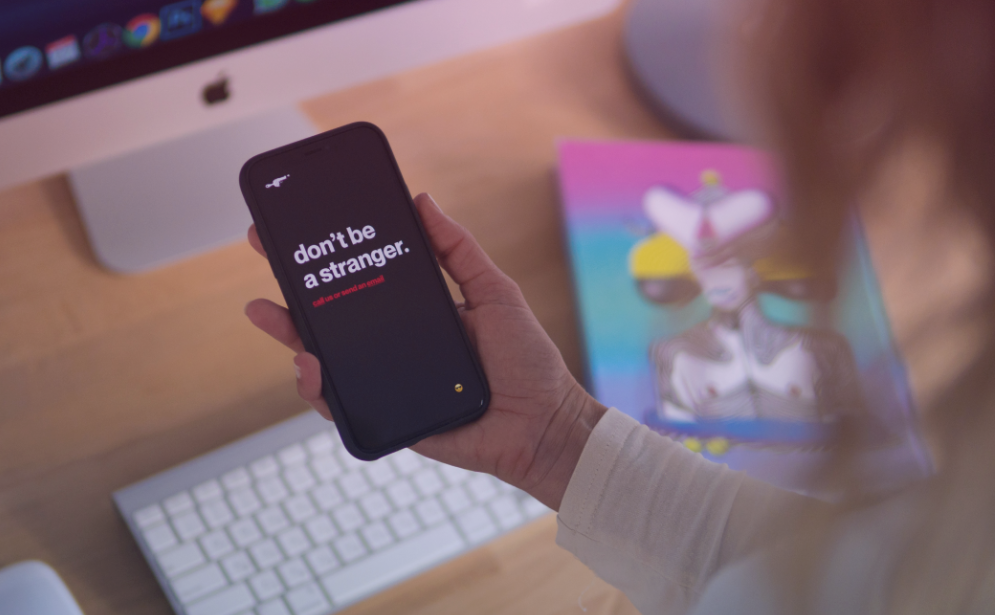 A woman holds a phone in her hand while working at a desk.