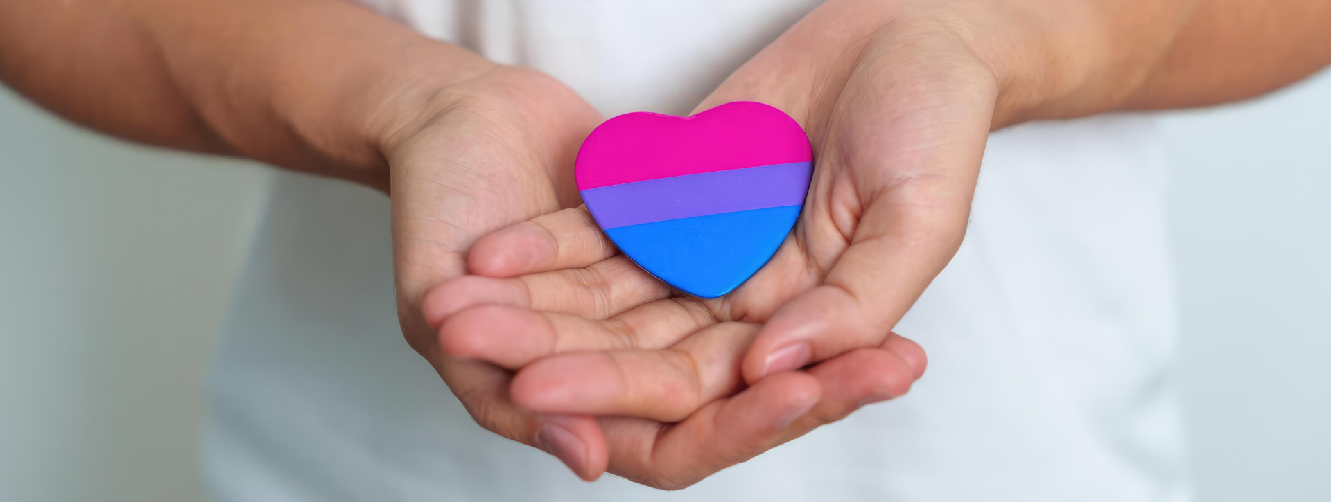 Hands holding a heart with the colours of the Bisexual flag