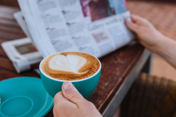 Person relaxing at a table with a latte and newspaper